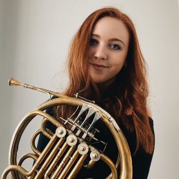 Hannah, with long red hair, holds her French horn