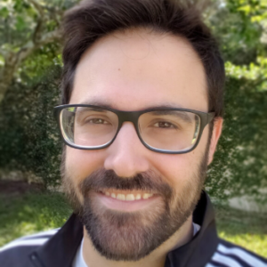 Jarod Roselló wearing glasses and smiling in front of a leafy green tree